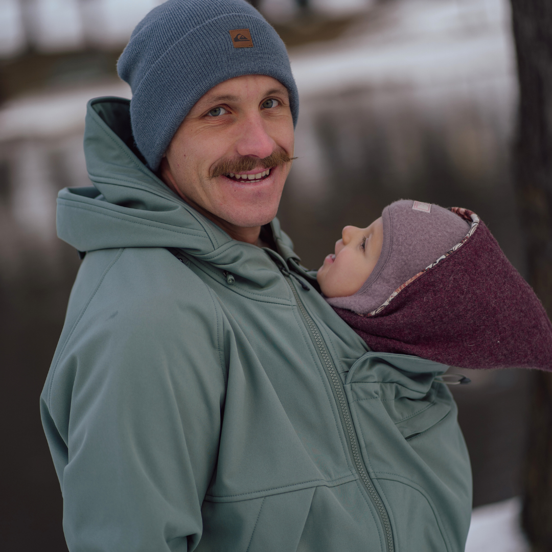 Father carrying baby in green softshell babywearing jacket, both warmly dressed outdoors