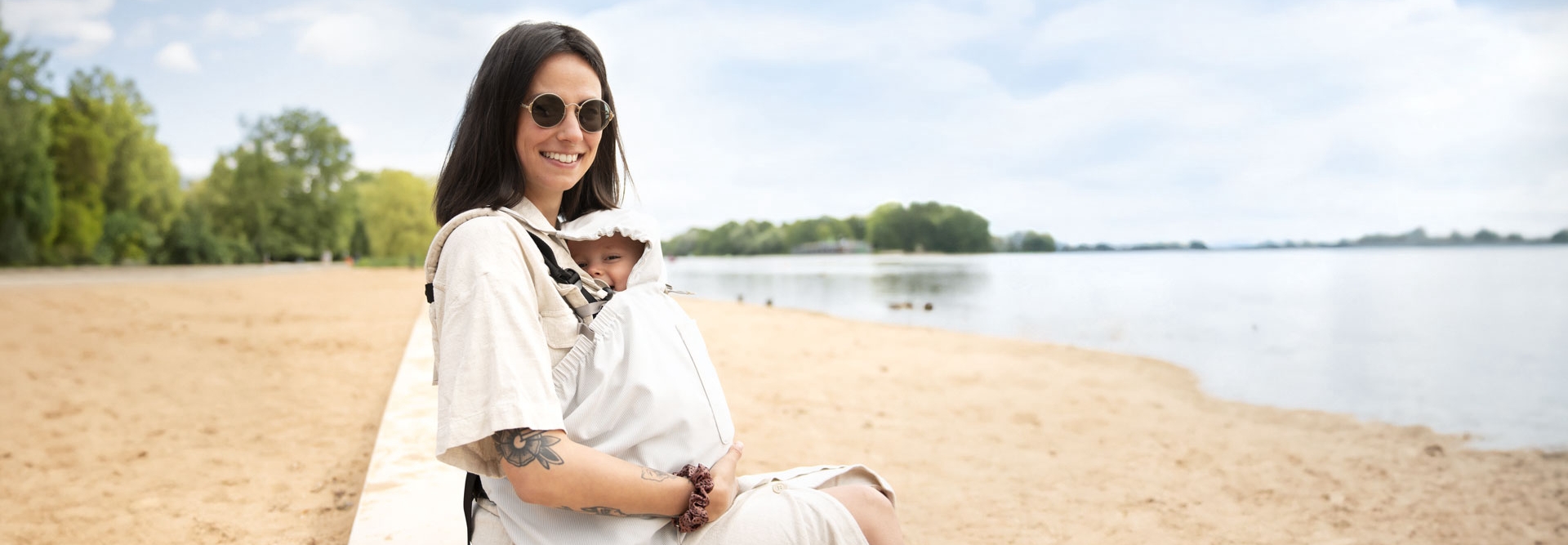 Woman sitting with baby under light sun cover on beach by water