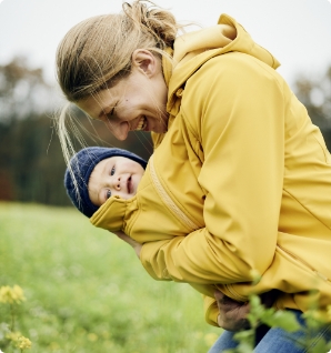 A young mother wearing a yellow softshell babywearing jacket with her baby.