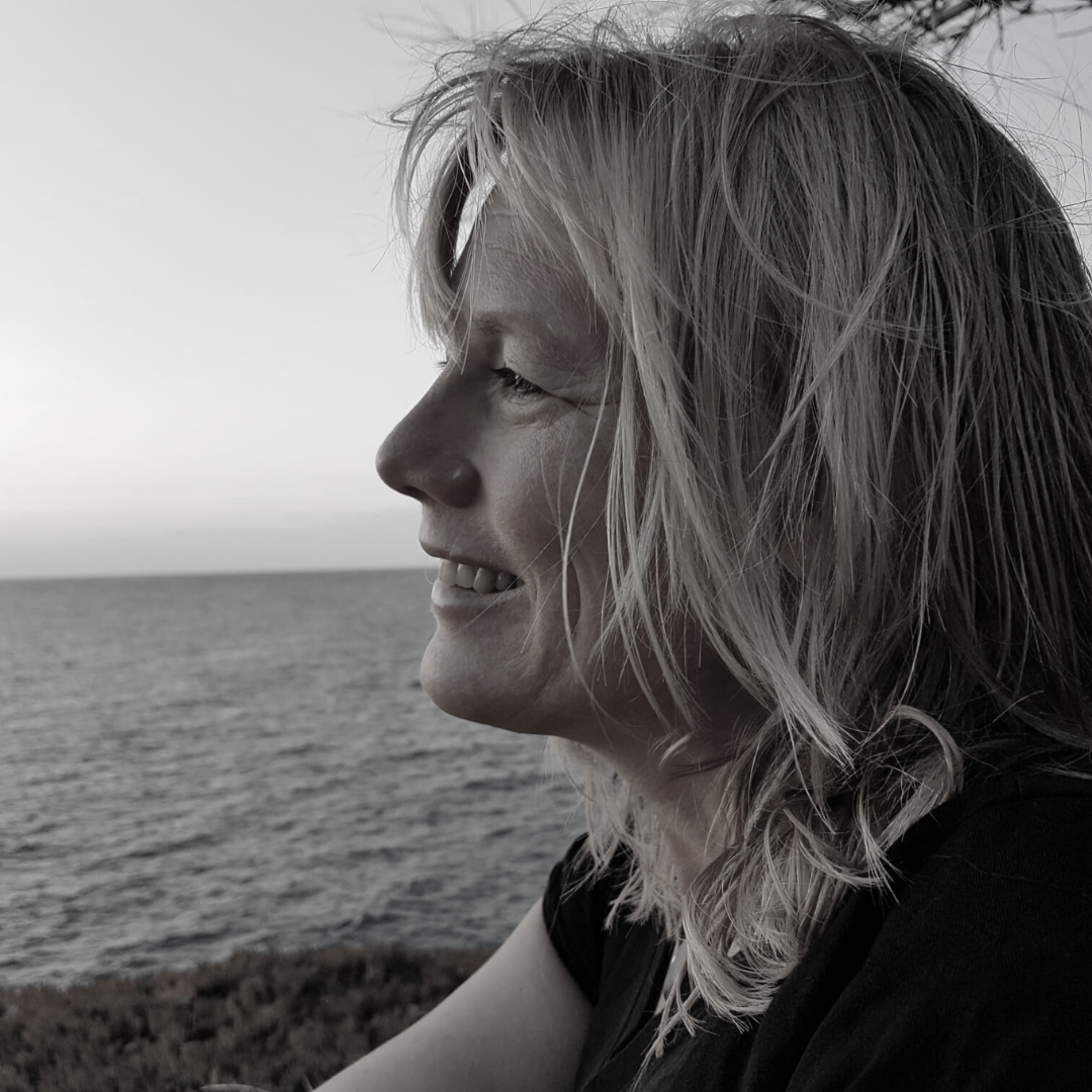 Portrait of woman by the sea, smiling in profile, windblown hair