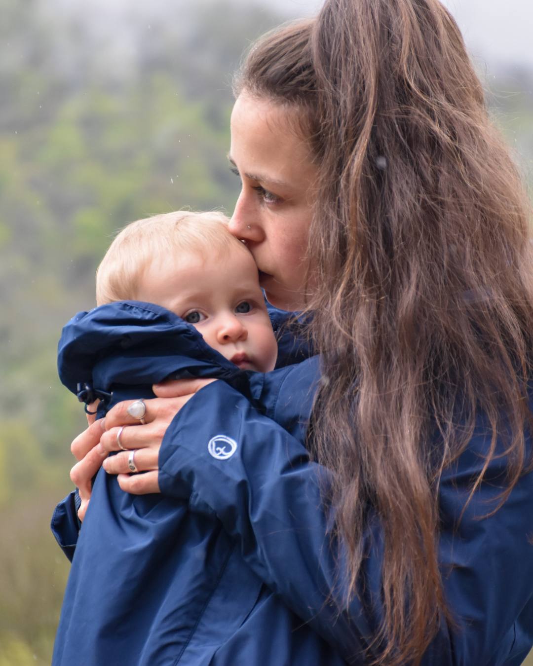 Mother cuddling baby in blue jacket, close-up portrait, tender outdoor moment