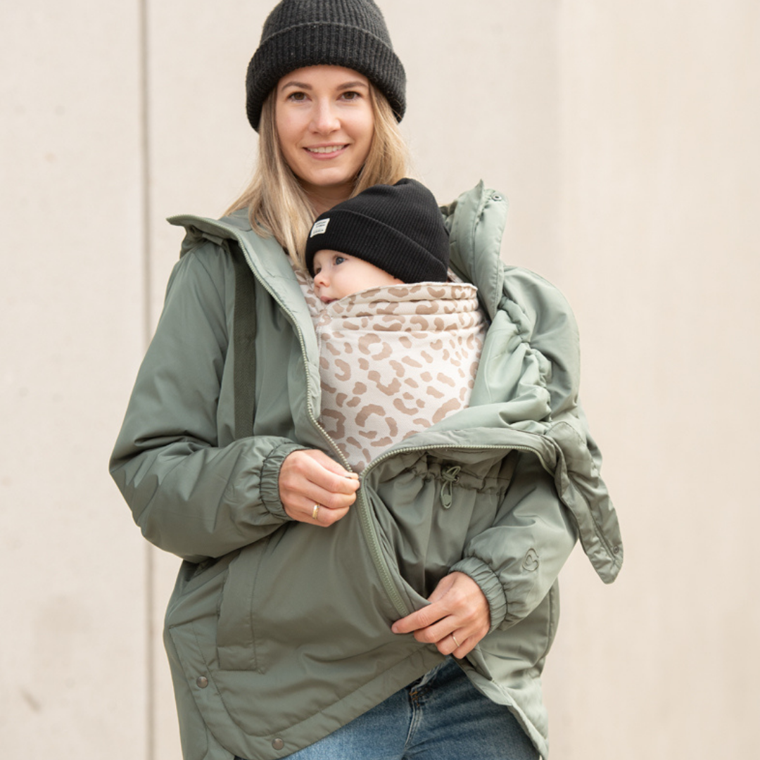 Mother carrying baby in green babywearing jacket with patterned insert, urban background
