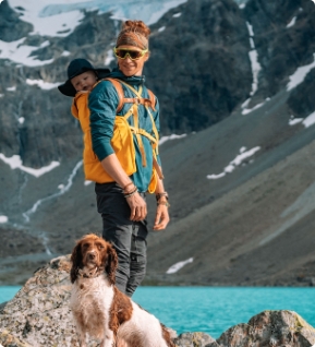 Father carrying baby on his back with dog by mountain lake, active outdoor scene