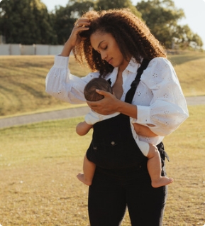 Mother carrying baby in black baby carrier on a meadow, tender outdoor moment