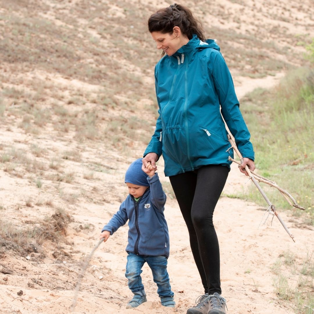 Pregnant woman in blue jacket walking with child in sandy landscape
