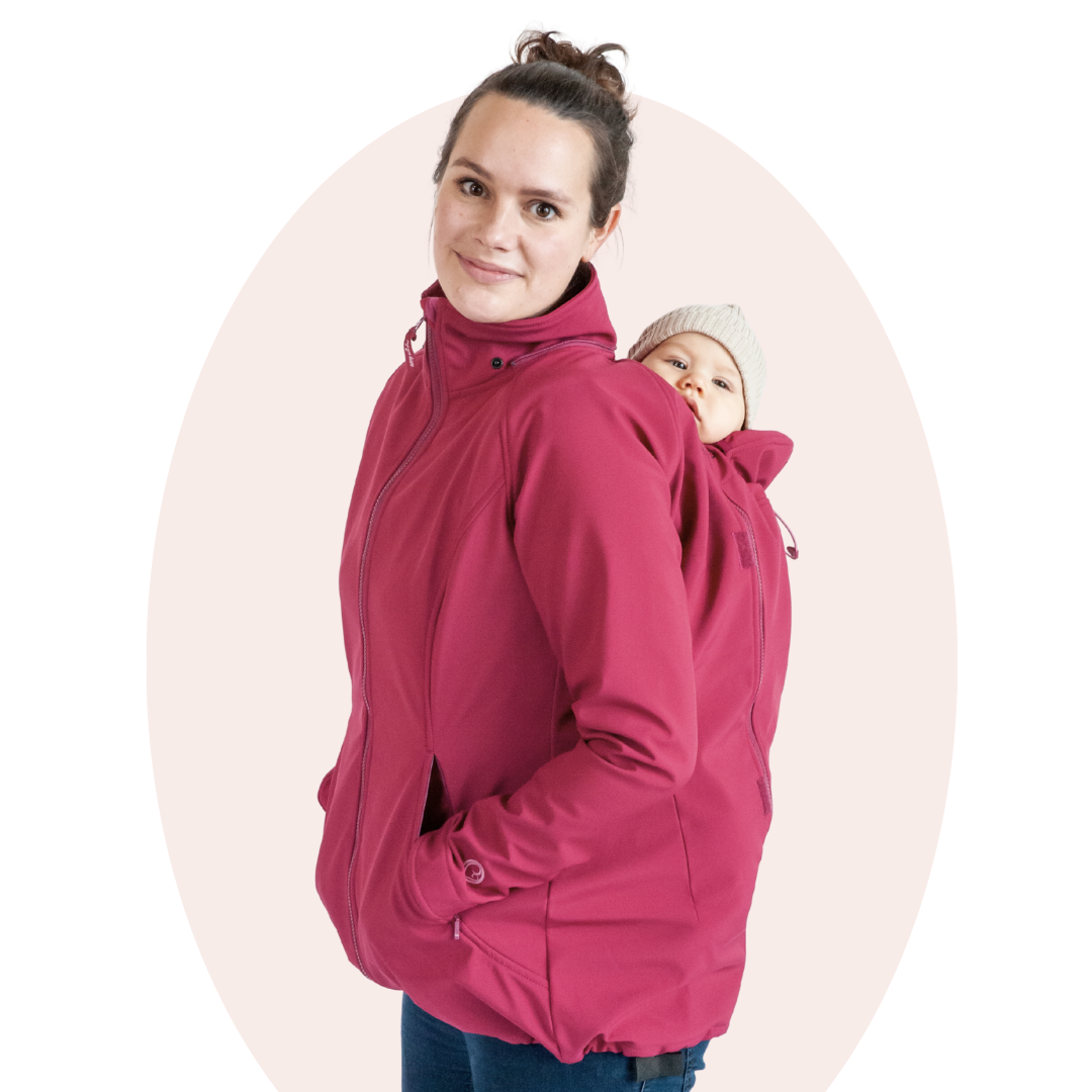 Mother carrying baby on her back in pink softshell babywearing jacket, studio setting
